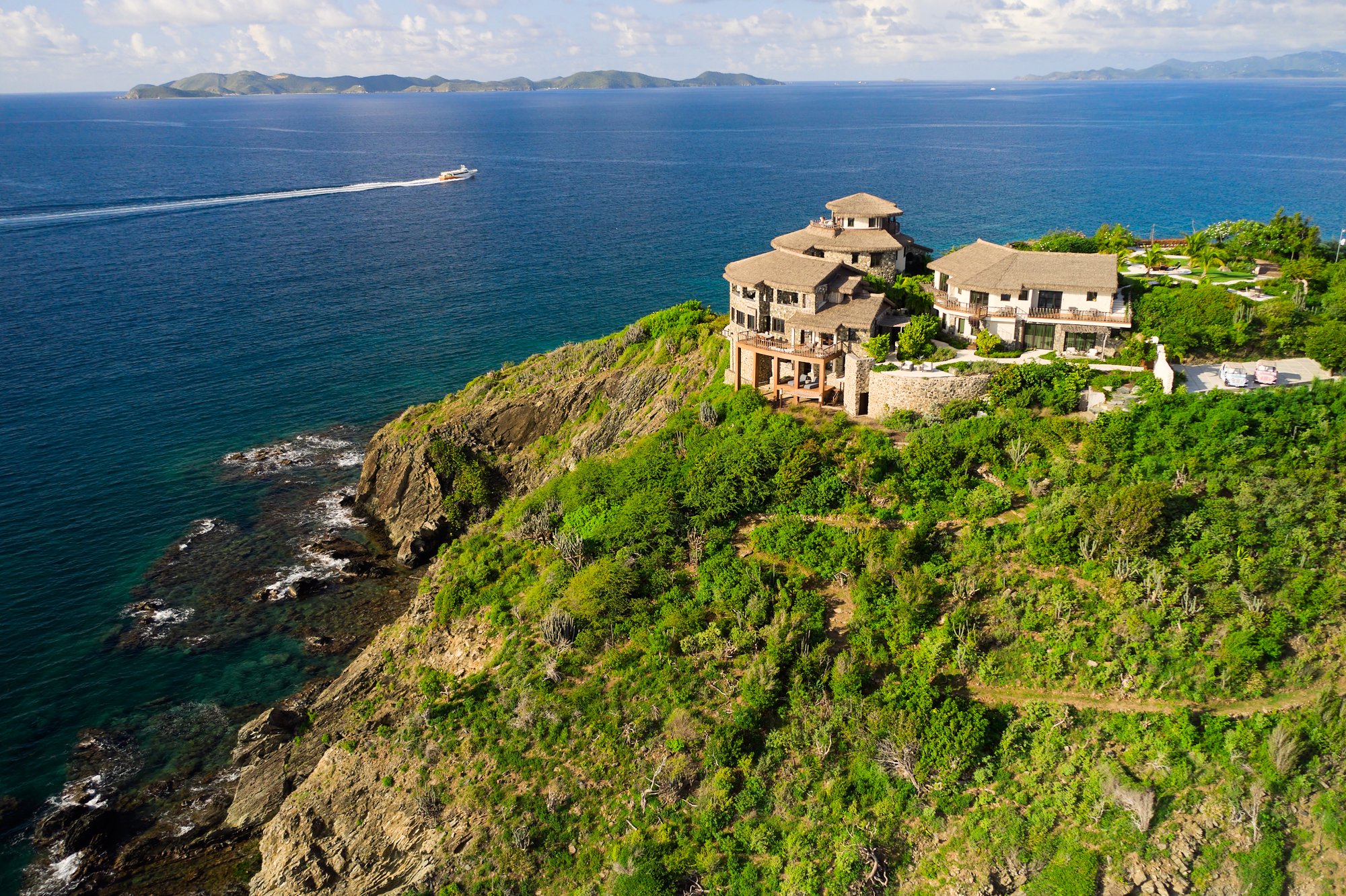 Aerial view of cliffside resort buildings with a boat approaching The Aerial, BVI