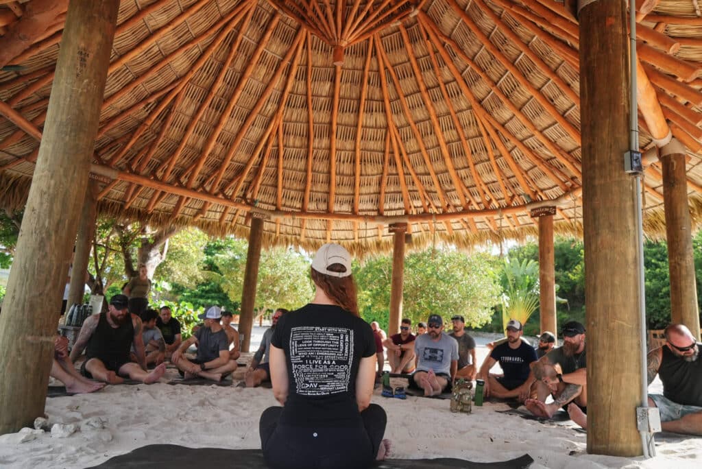 Veterans and first responders sit in a guided meditation circle beneath an open-air pavilion on the beach.