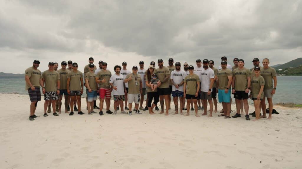 A group of veterans, first responders, and facilitators stand together on the beach during a Heal the Heroes retreat.