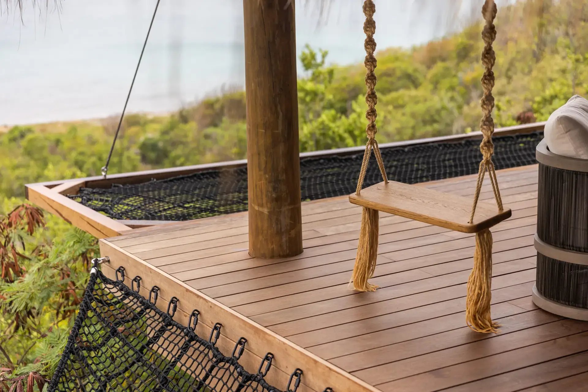 Wooden swing on a deck overlooking the treetops and ocean.