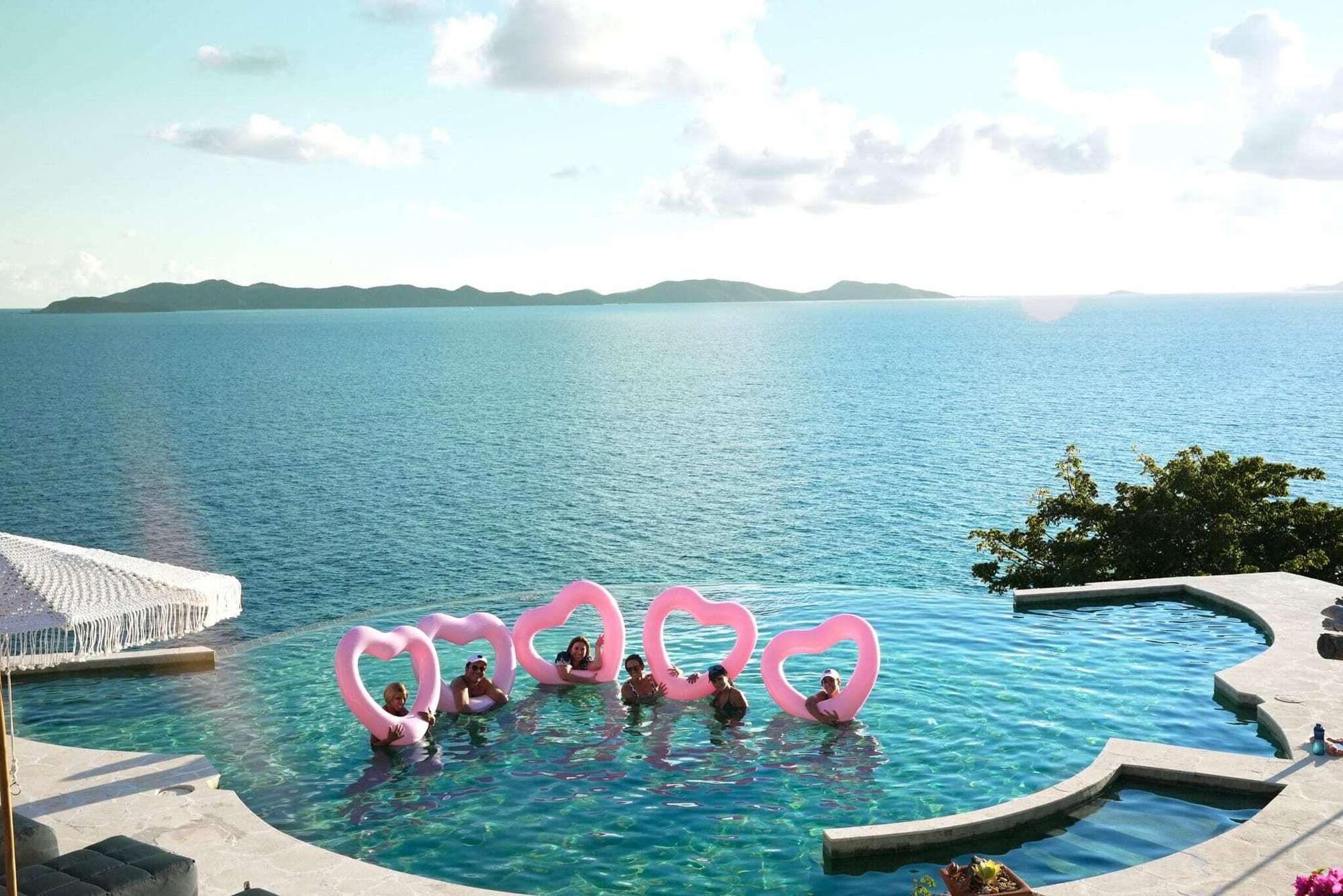 Aerial view of an infinity pool with pink flamingo floats overlooking the ocean