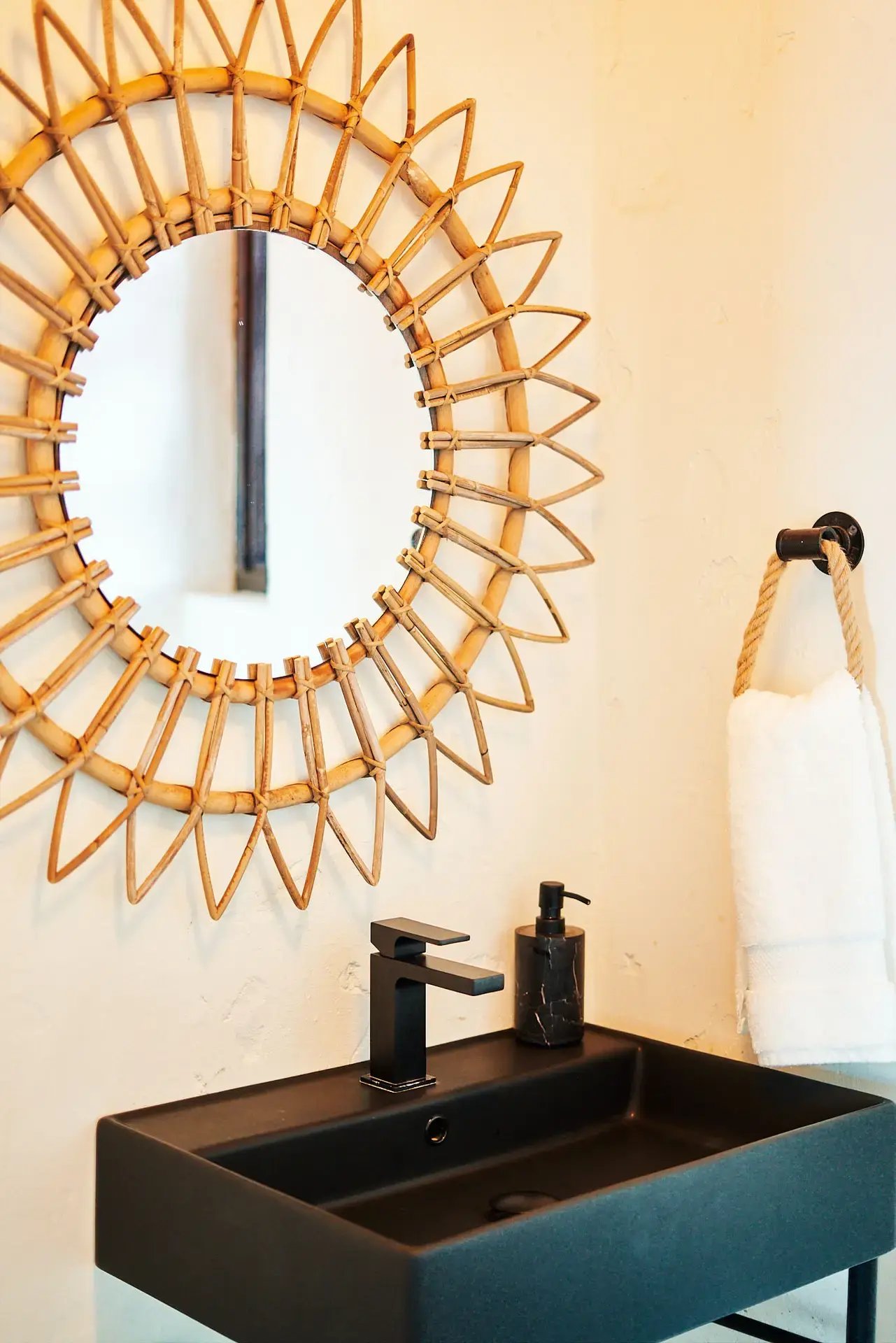 Bathroom sink with woven rattan mirror and black fixtures.