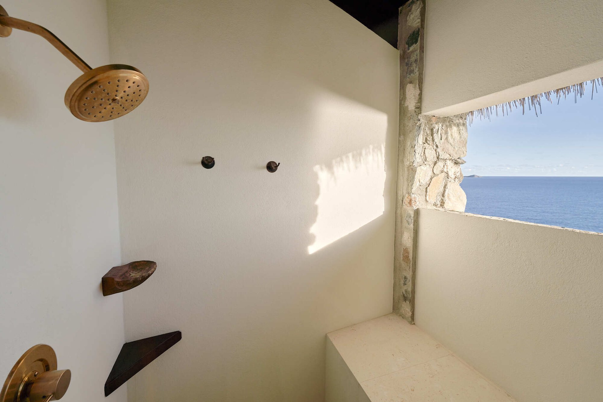 Outdoor-style shower with gold fixtures and ocean-view window.