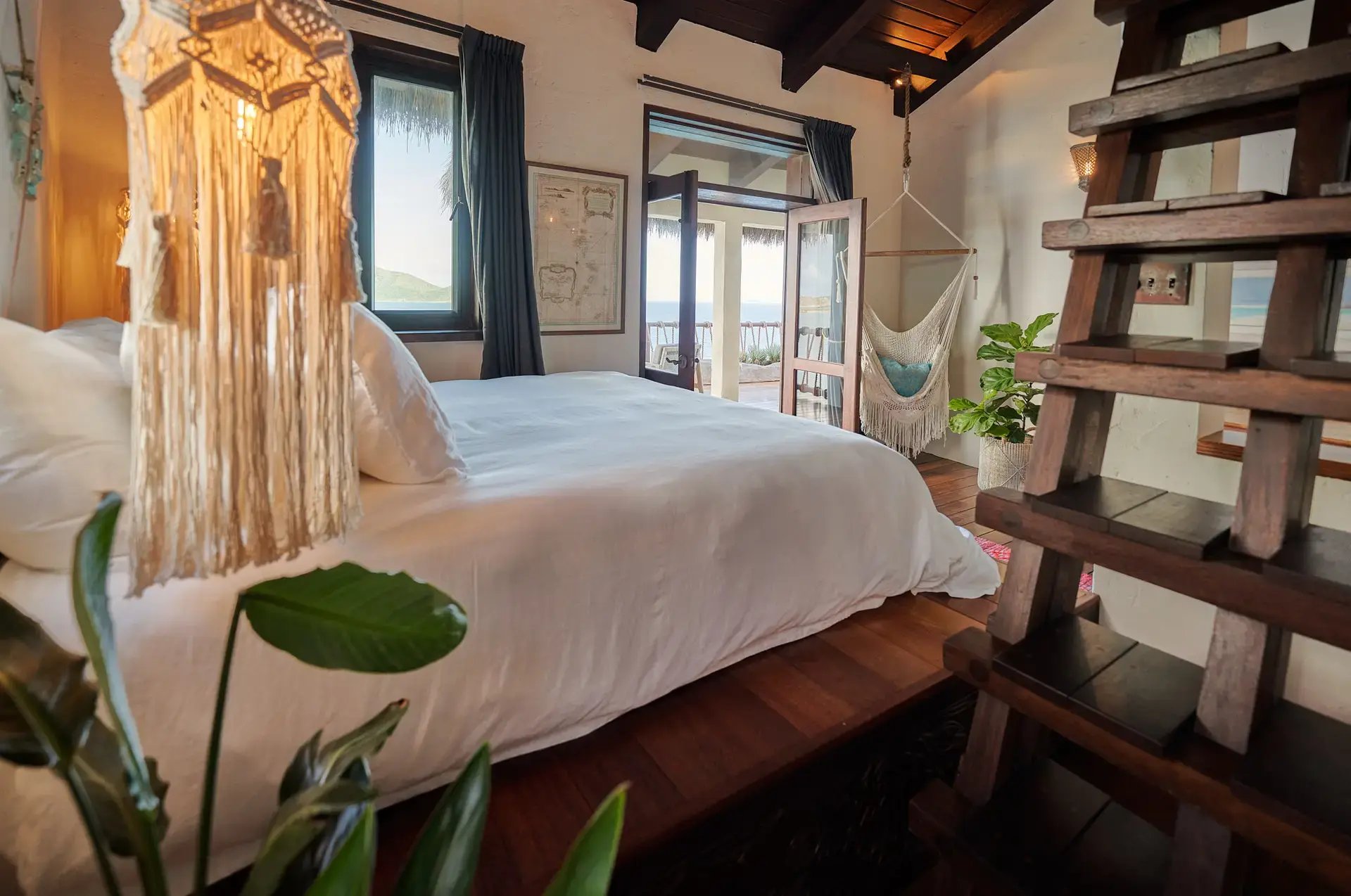 Bedroom with macramé pendant light, hammock, and ocean view.