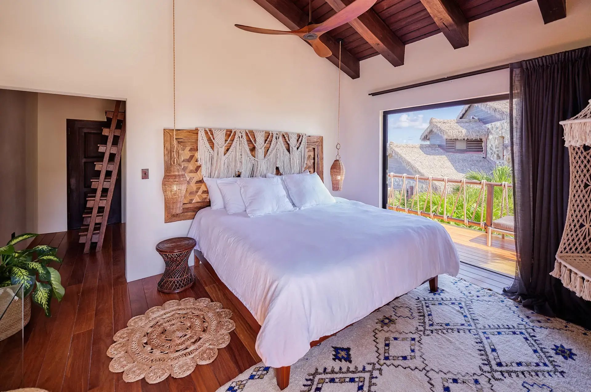Bedroom with macramé headboard, ladder loft, and ocean-view balcony.
