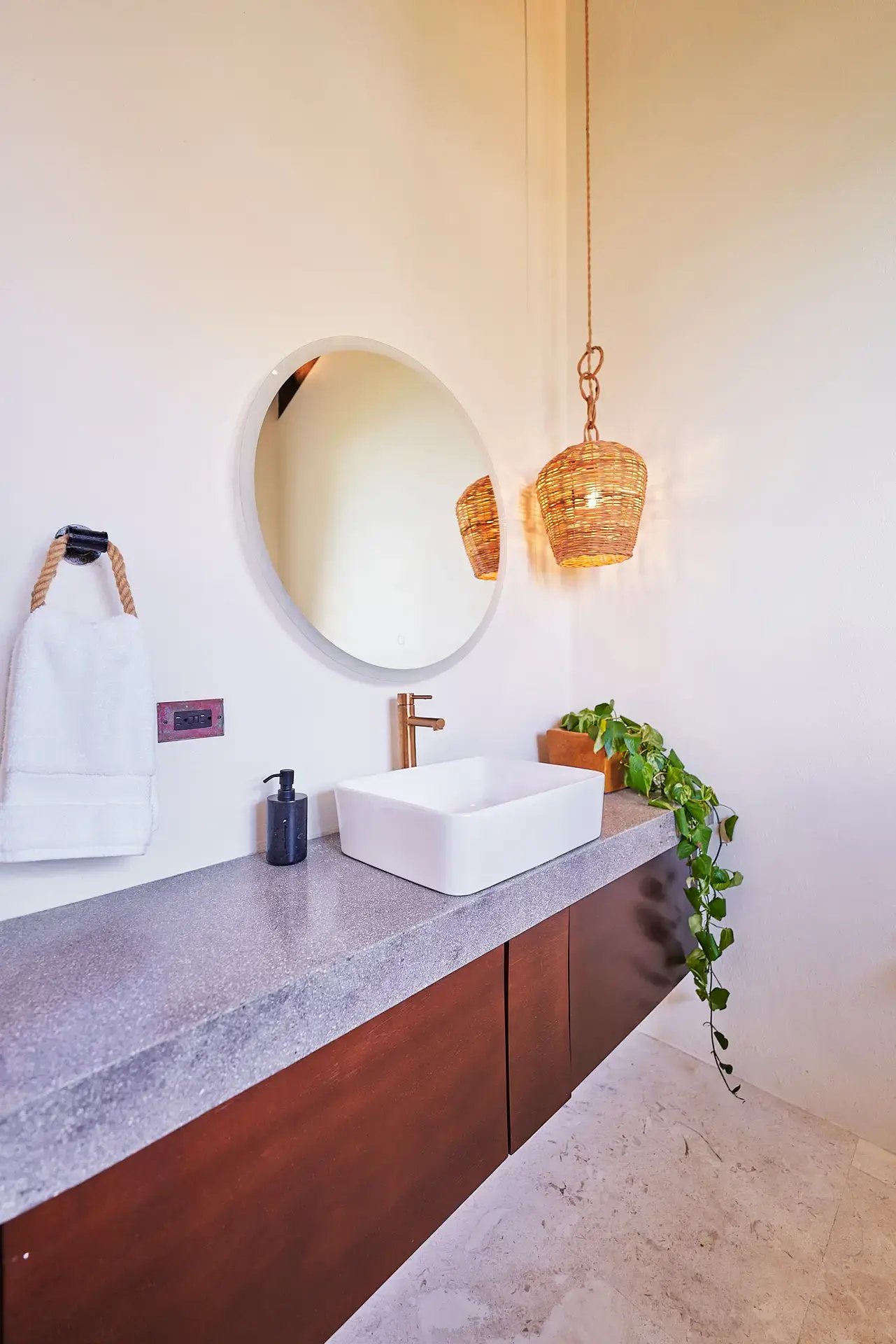 Bathroom sink with round mirror and hanging rattan lights.
