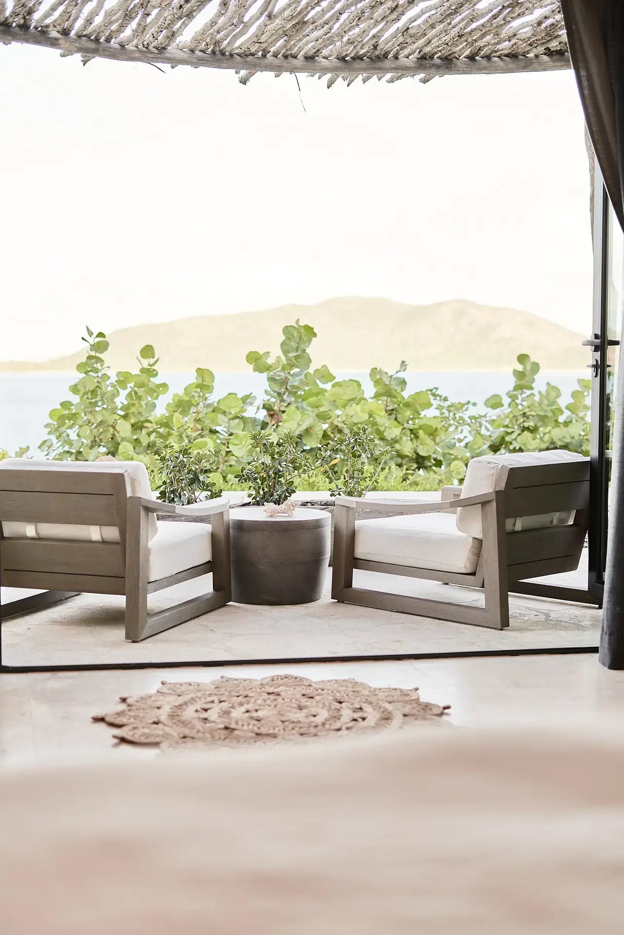 Covered patio with two lounge chairs overlooking greenery.