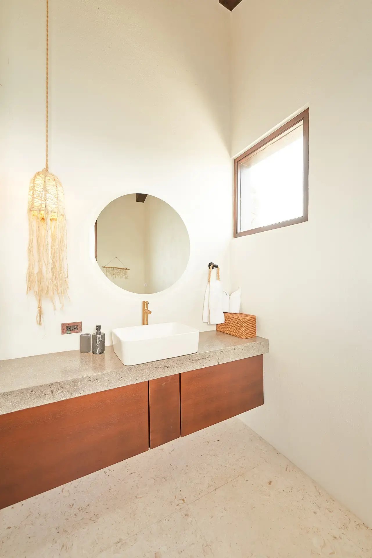 Bathroom vanity with round mirror and macramé pendant light.