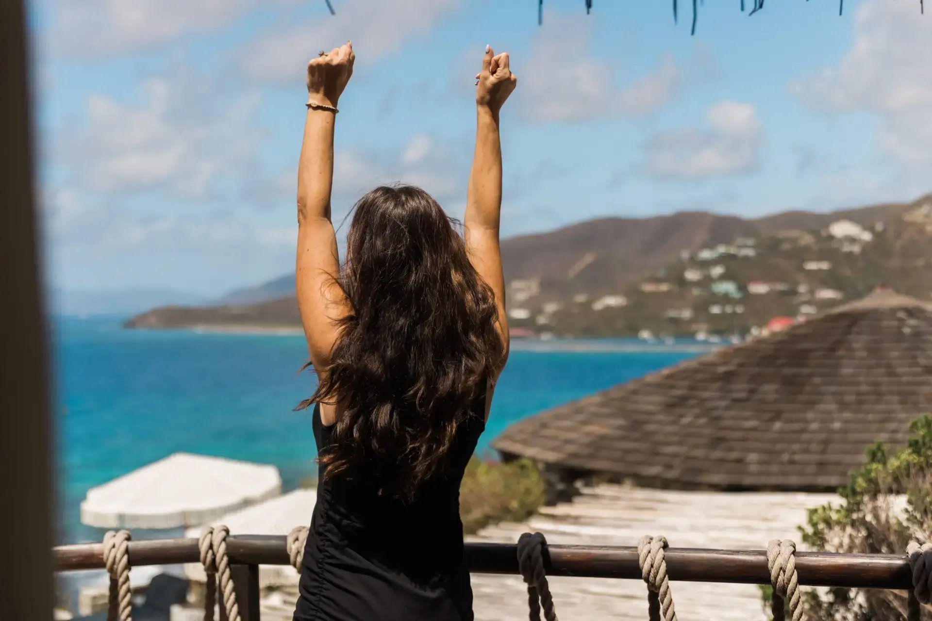 Woman with arms raised overlooking the island and coastline from a balcony