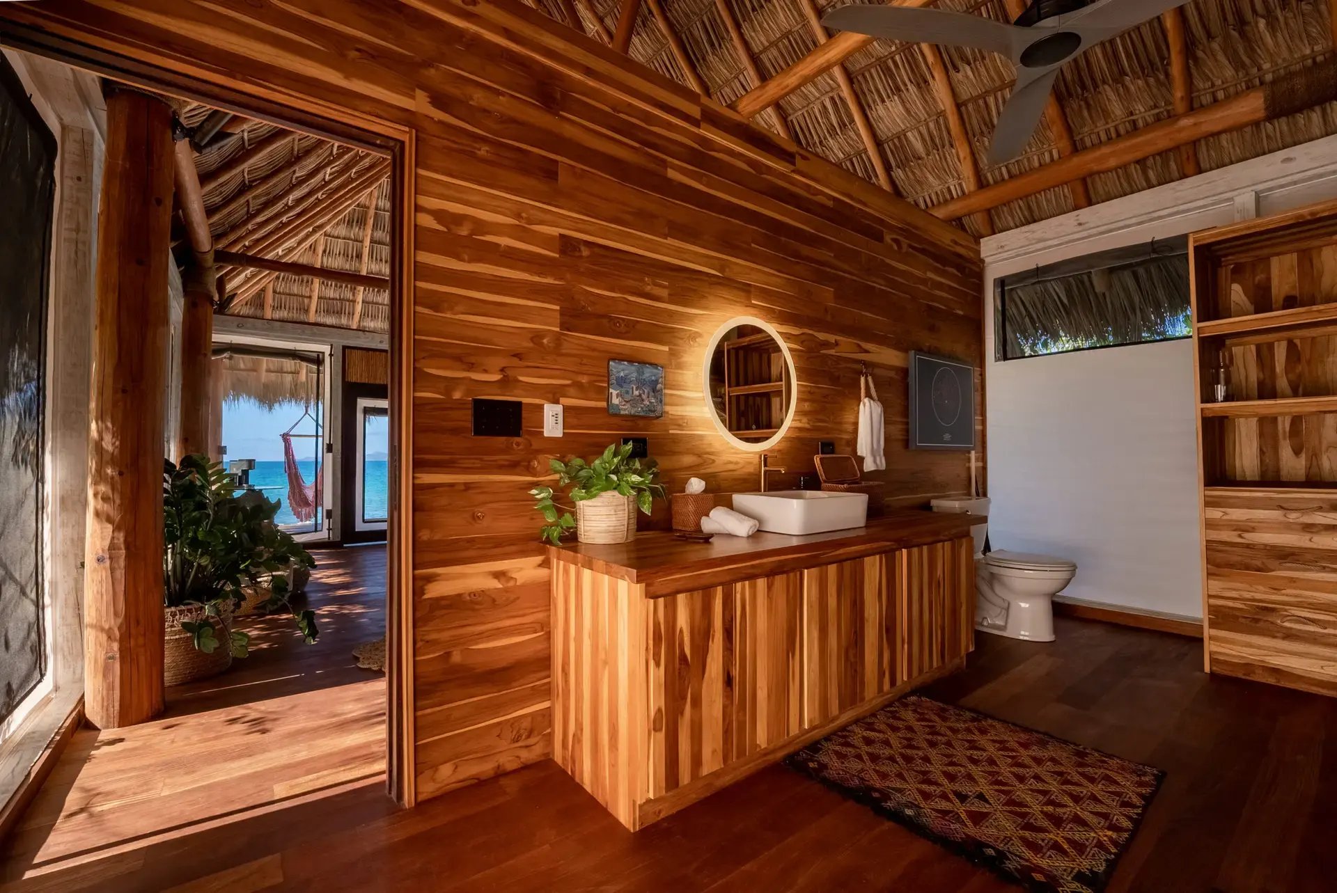 Wood-paneled bathroom with round mirror and ocean-view doorway.