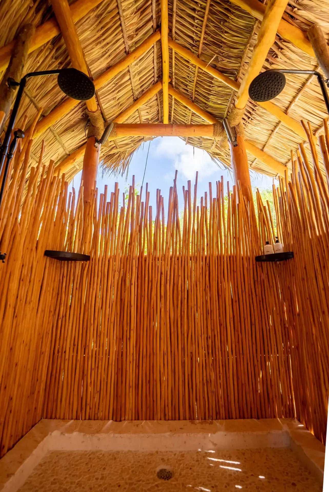 Bamboo-walled outdoor shower with open thatched roof.