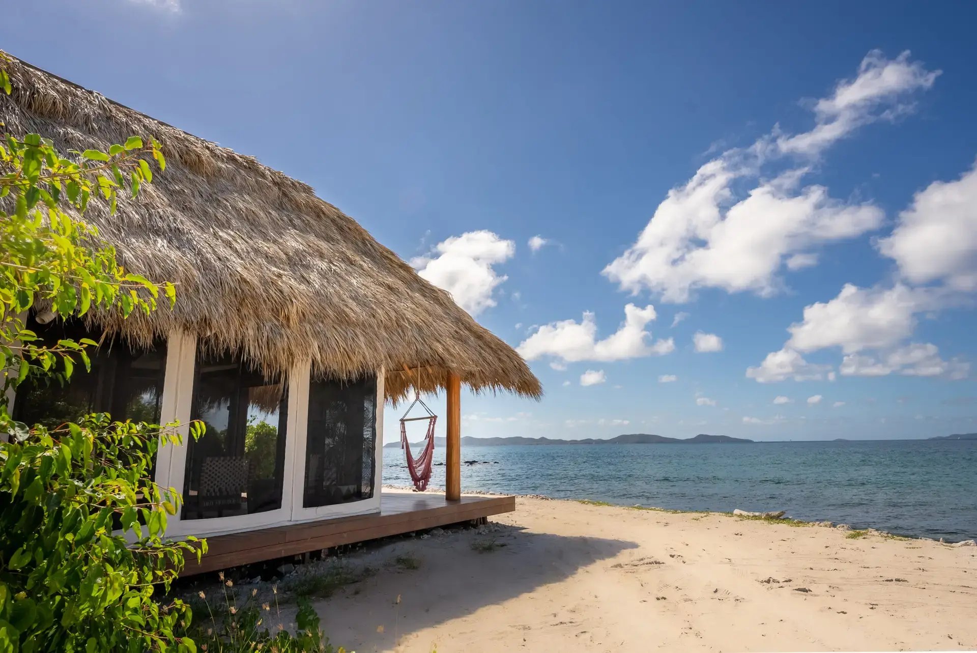 Beachside cabana with hammock chair steps from the shore.