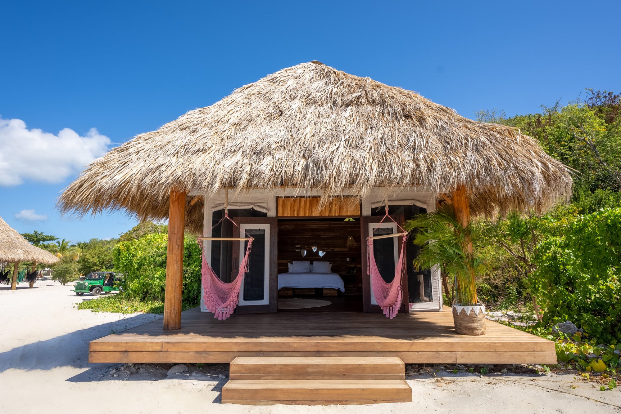 Thatched-roof beach bungalow with pink hammock chairs on the porch.