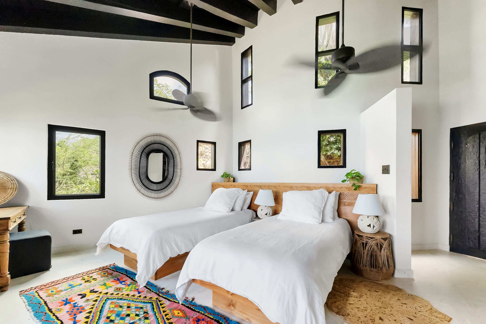 Twin bedroom with high beamed ceiling and round mirror.