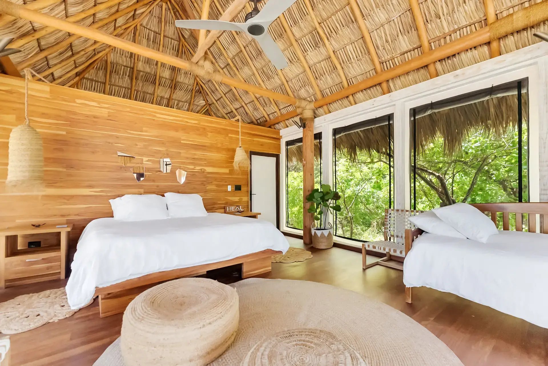 Twin beds in a wood-paneled room with thatched roof and forest view.