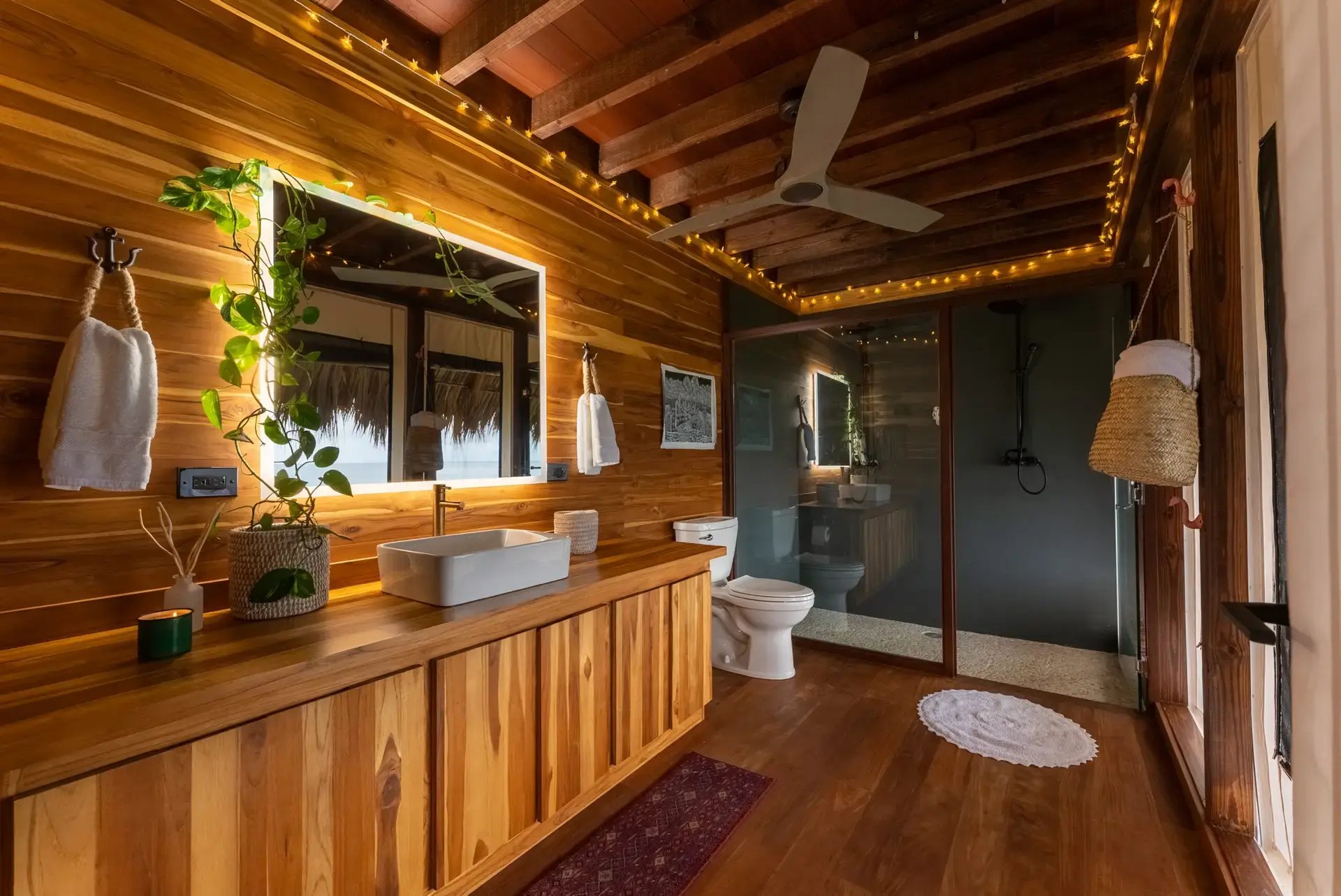 Wood-paneled bathroom with glass shower and string lights.