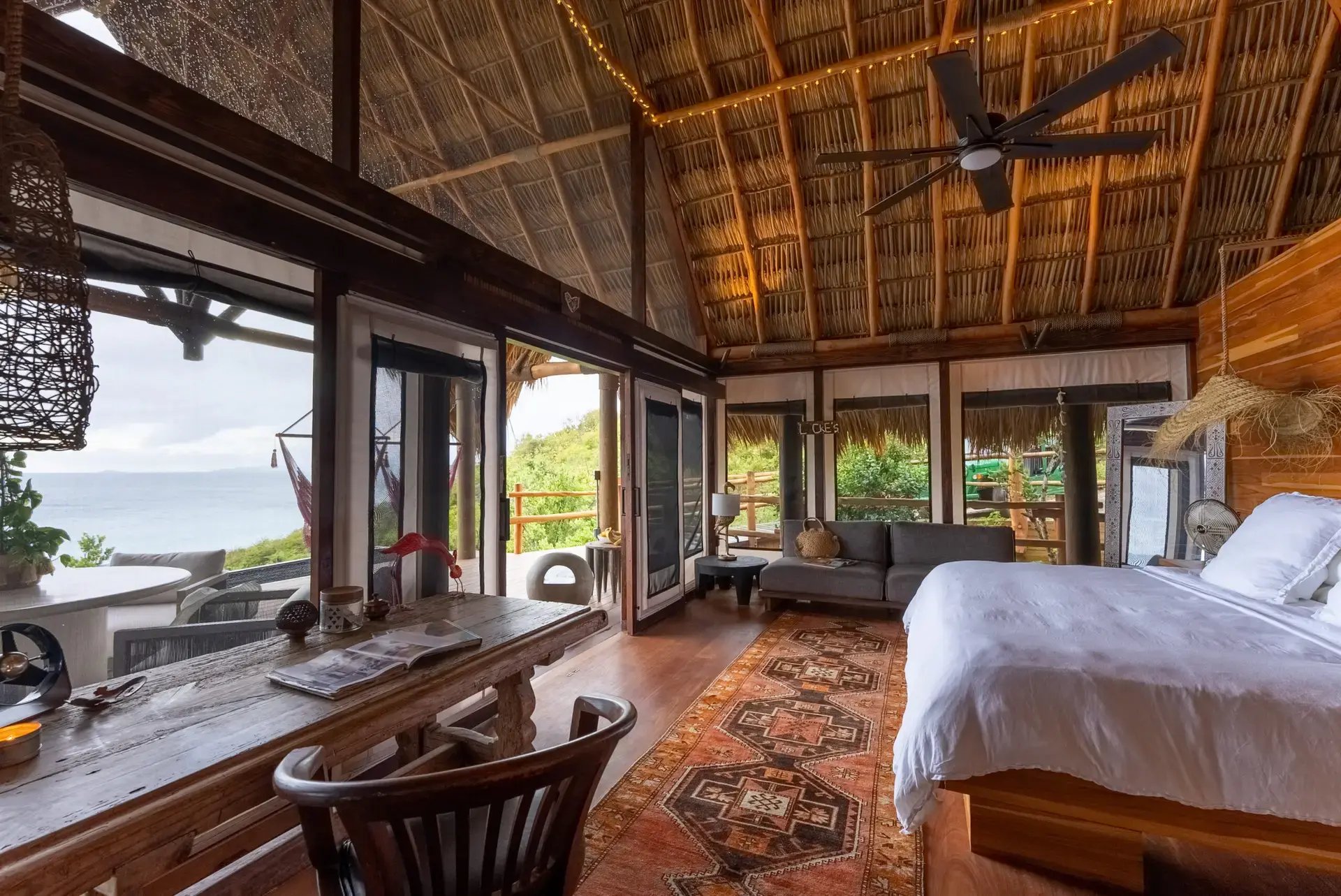 Open-air living and sleeping area with thatched roof and jungle view.