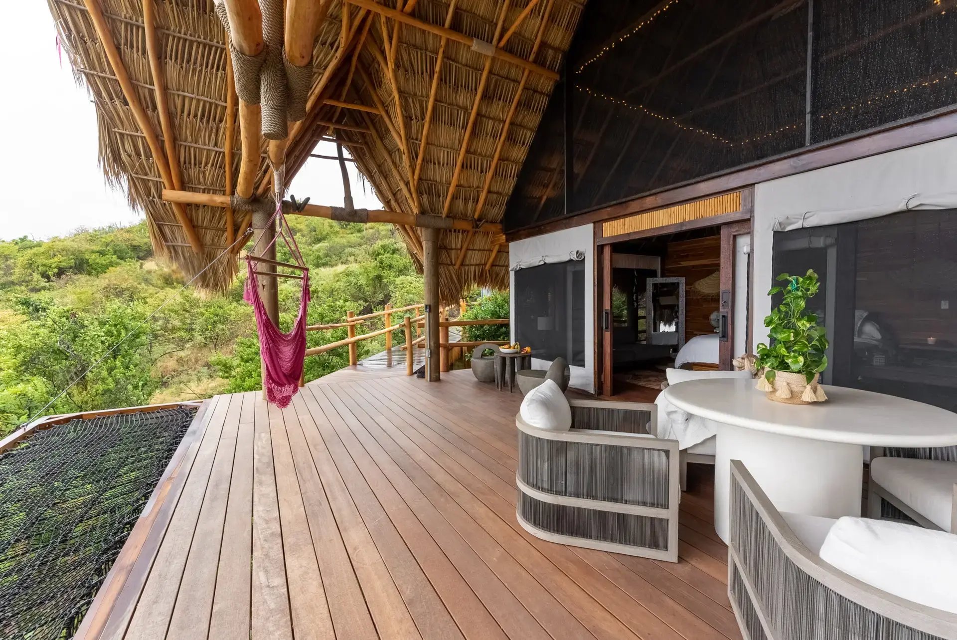 Thatched-roof deck with hanging hammock chair and lounge seating.