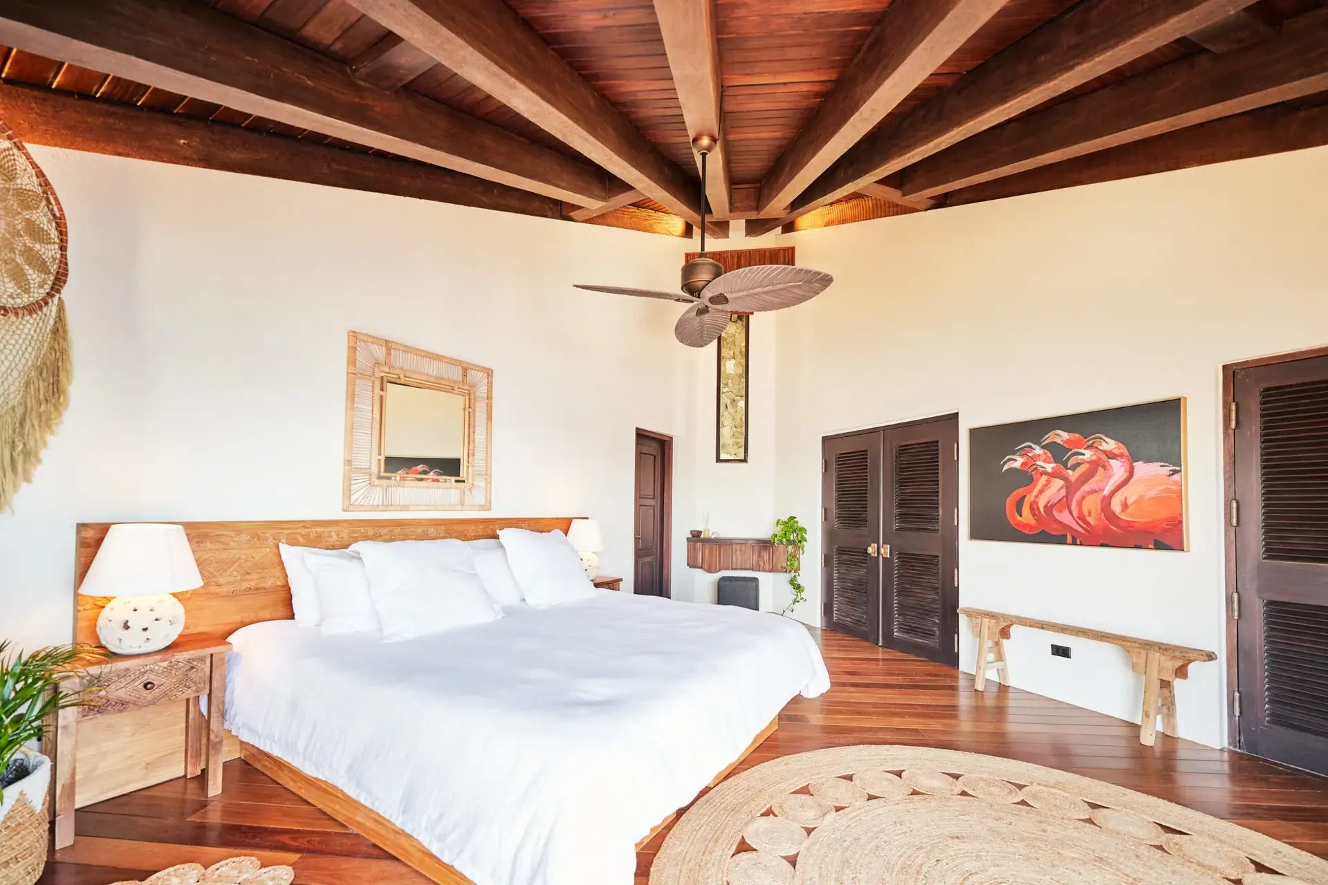 Bedroom with carved wood bed, rattan mirror, and flamingo artwork.