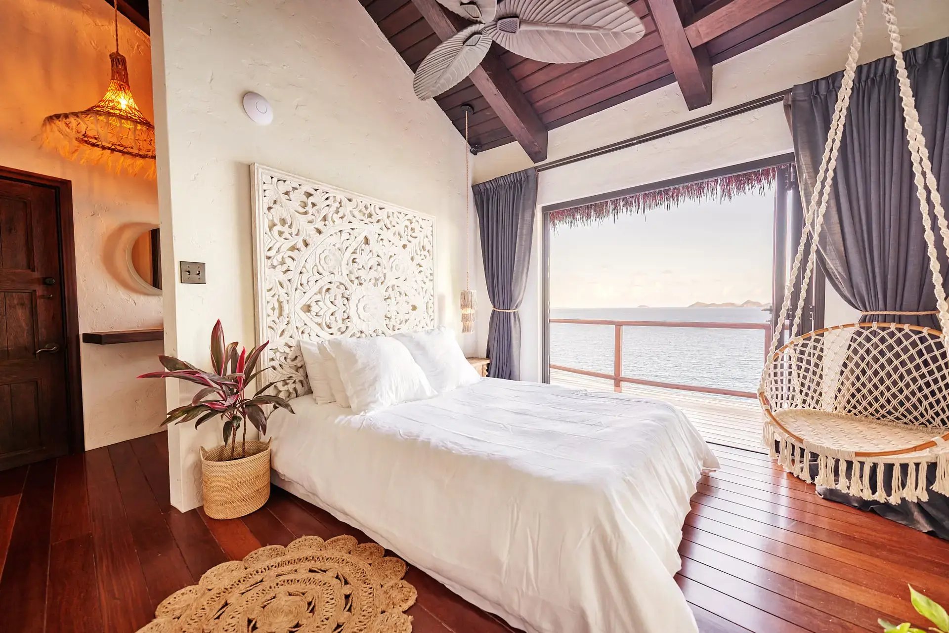 Overwater-style bedroom with carved headboard, hanging chair, and ocean view.
