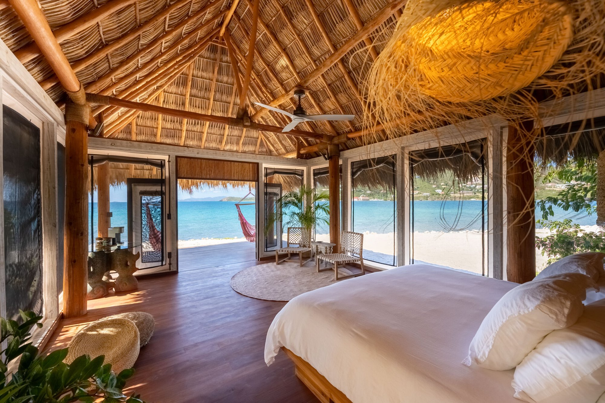 Beachfront bedroom under a thatched roof with ocean view.
