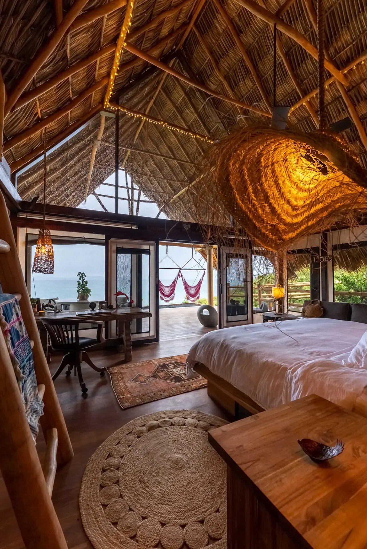 Open-plan bedroom with ocean view under a thatched ceiling.