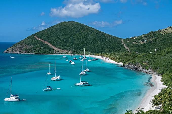 Aerial view of a lush green island with sailboats anchored in a turquoise bay