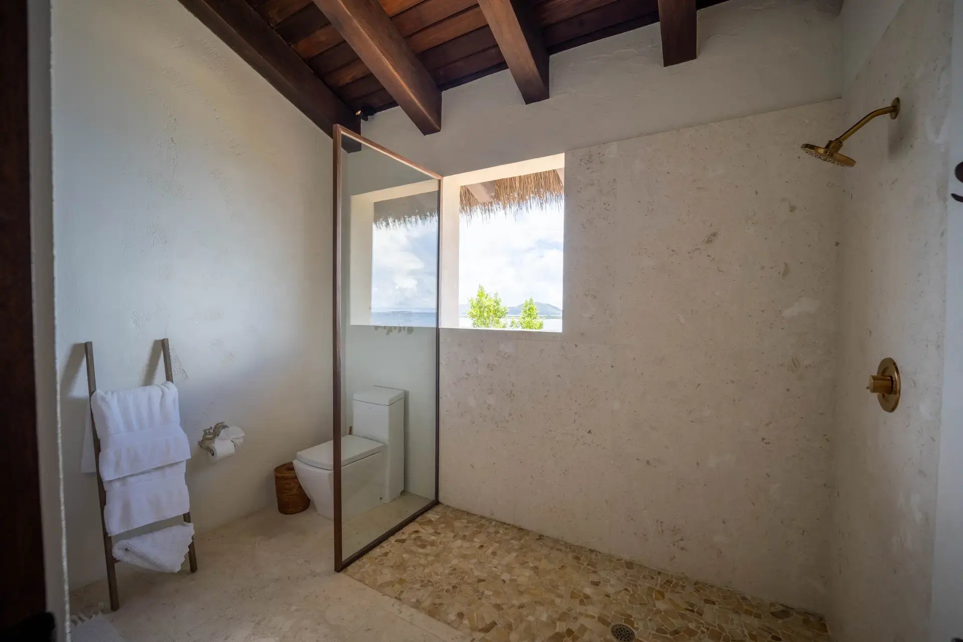 Open-air bathroom with glass shower and exposed wood beams.