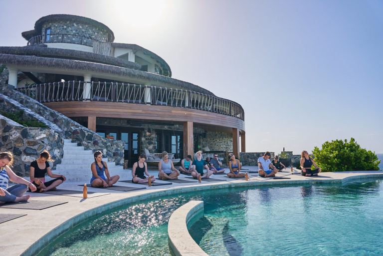 Guests doing yoga poolside at a resort building overlooking the ocean
