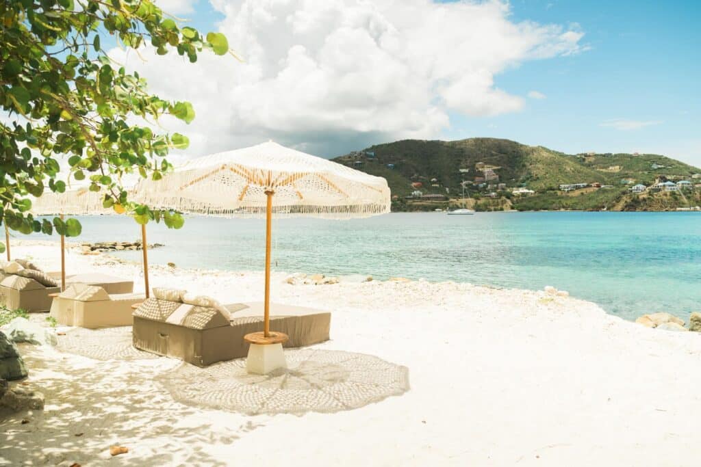 Shaded beach loungers with woven umbrellas facing turquoise Caribbean water.