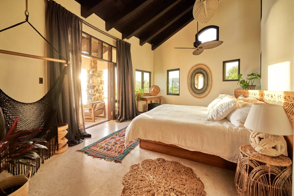 Cozy villa bedroom with wood accents, woven decor, and sunlight streaming through the balcony doors.