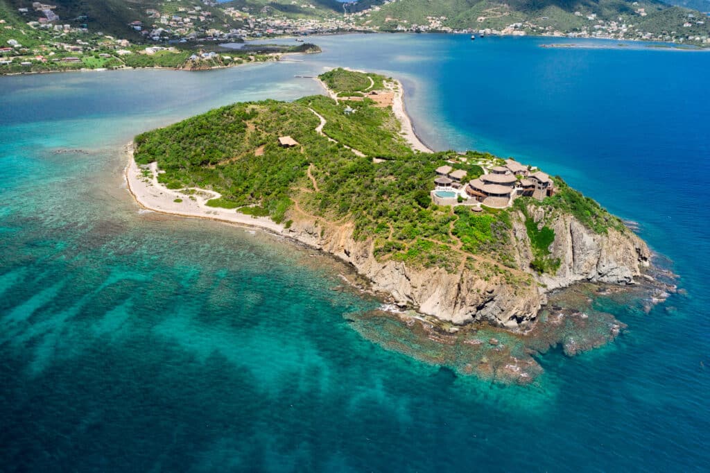 Aerial view of Buck Island showing rugged cliffs, turquoise reefs, and luxury villas overlooking the Caribbean Sea.