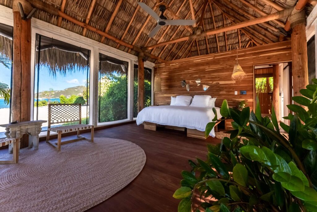 Spacious villa bedroom with wood walls, thatched ceiling, large windows, and ocean views at The Aerial BVI.