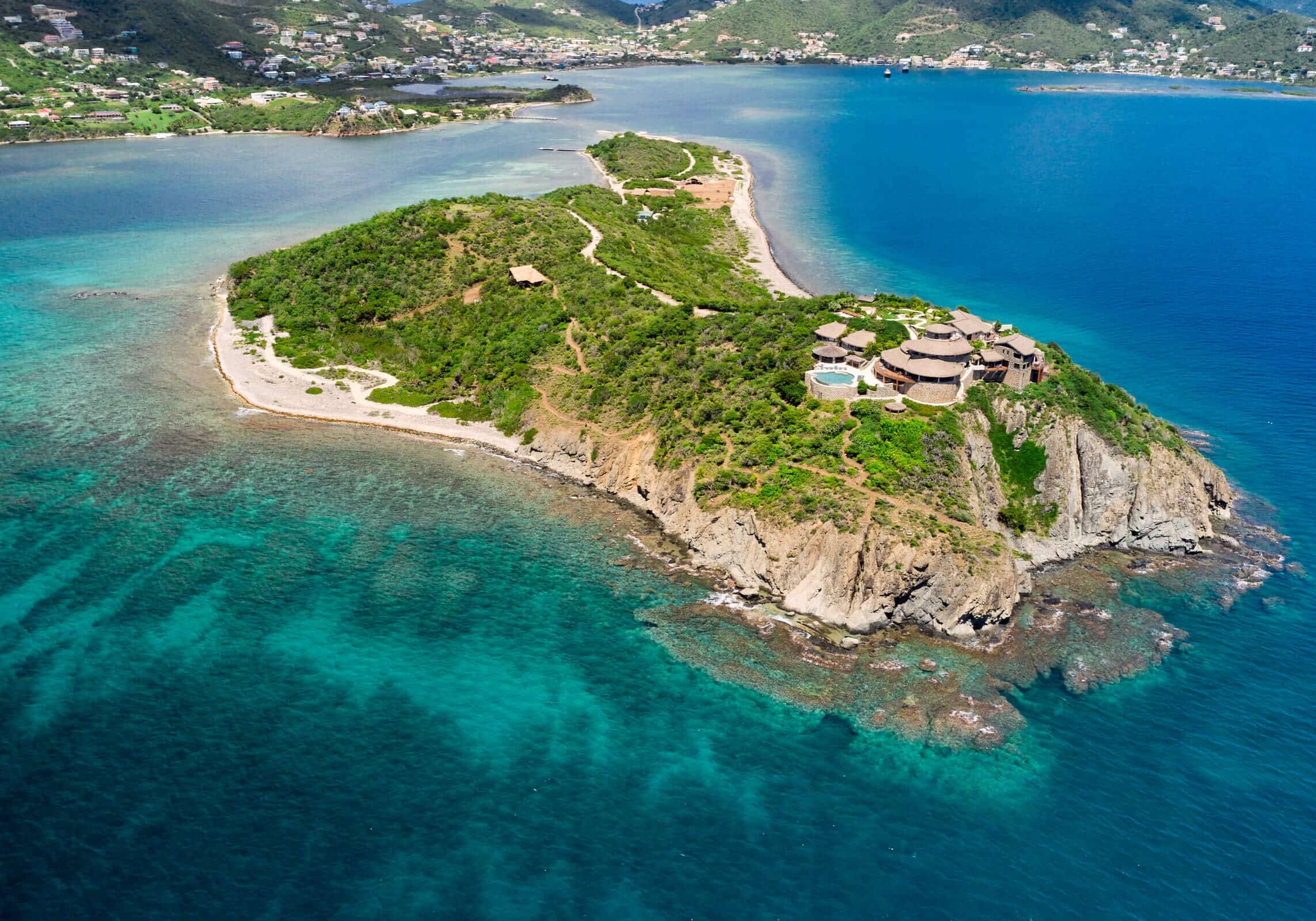 Aerial view of Buck Island showing rugged cliffs, turquoise reefs, and luxury villas overlooking the Caribbean Sea.
